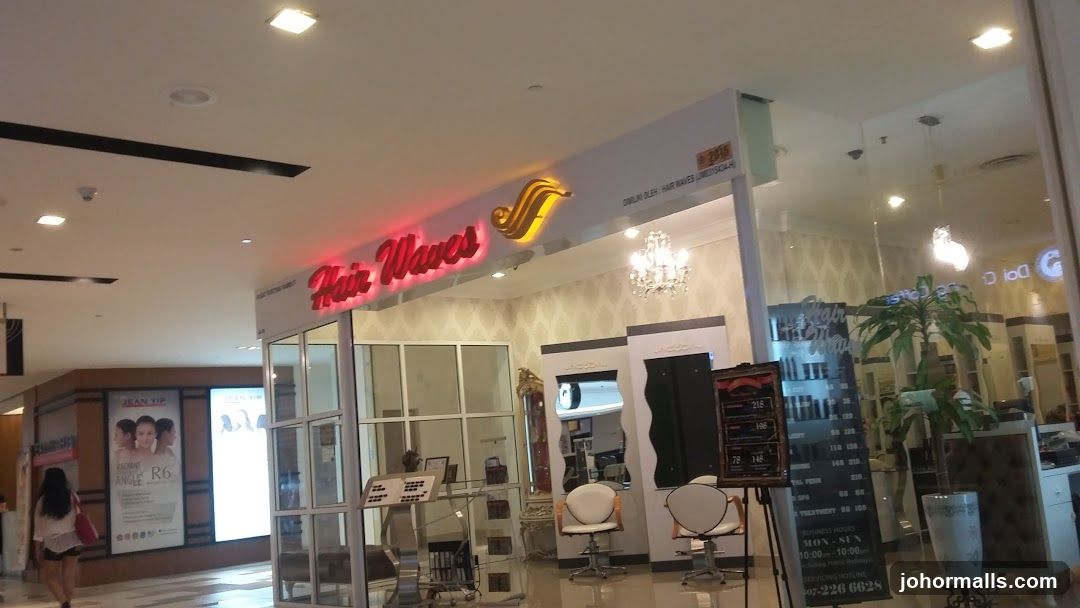 Storefront with illuminated red neon sign reading 'Hair Waves' and a stylized golden logo above the entrance. Glass doors and windows display interior styling chairs, mirrors, and chandeliers. A small sign on the wall indicates location number 218. The shop appears to be in a shopping mall with other stores nearby.