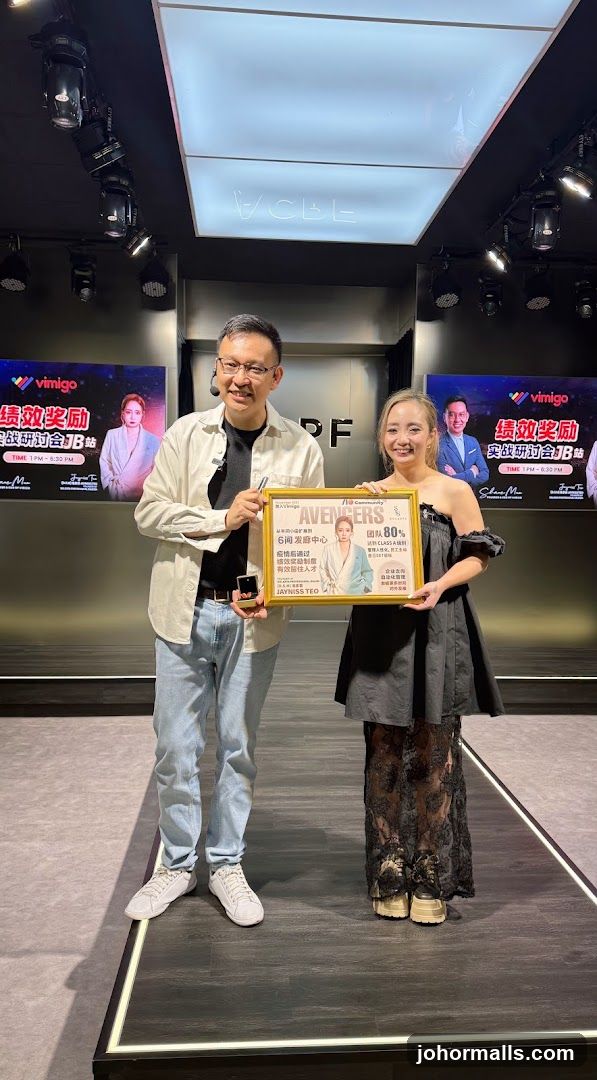 Two individuals holding a framed promotional poster