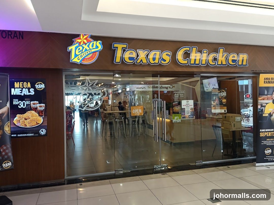 The exterior of a Texas Chicken restaurant with large glass doors and windows. The prominent Texas Chicken logo and name are displayed above the entrance. To the left, a poster advertises "Mega Meals" starting from RM30.90. Inside, tables and chairs are visible, along with customers and staff.