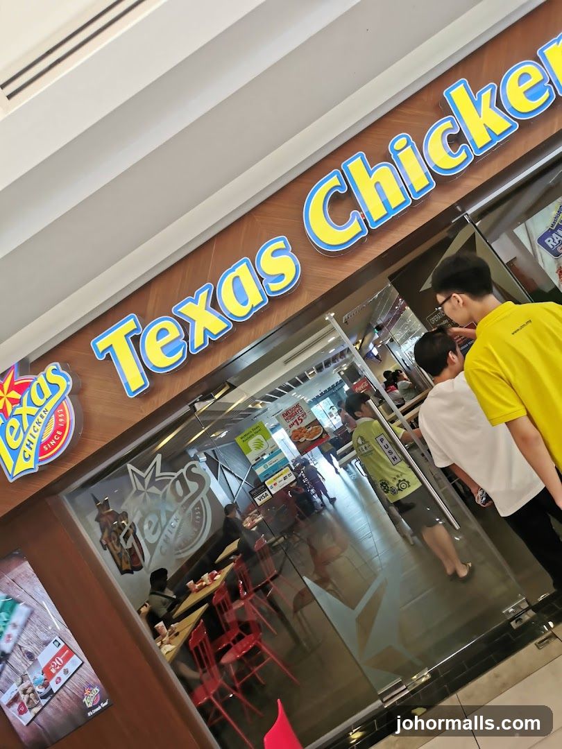The exterior of a Texas Chicken restaurant with large signage above the entrance. The glass doors reflect the interior, showing tables and chairs.