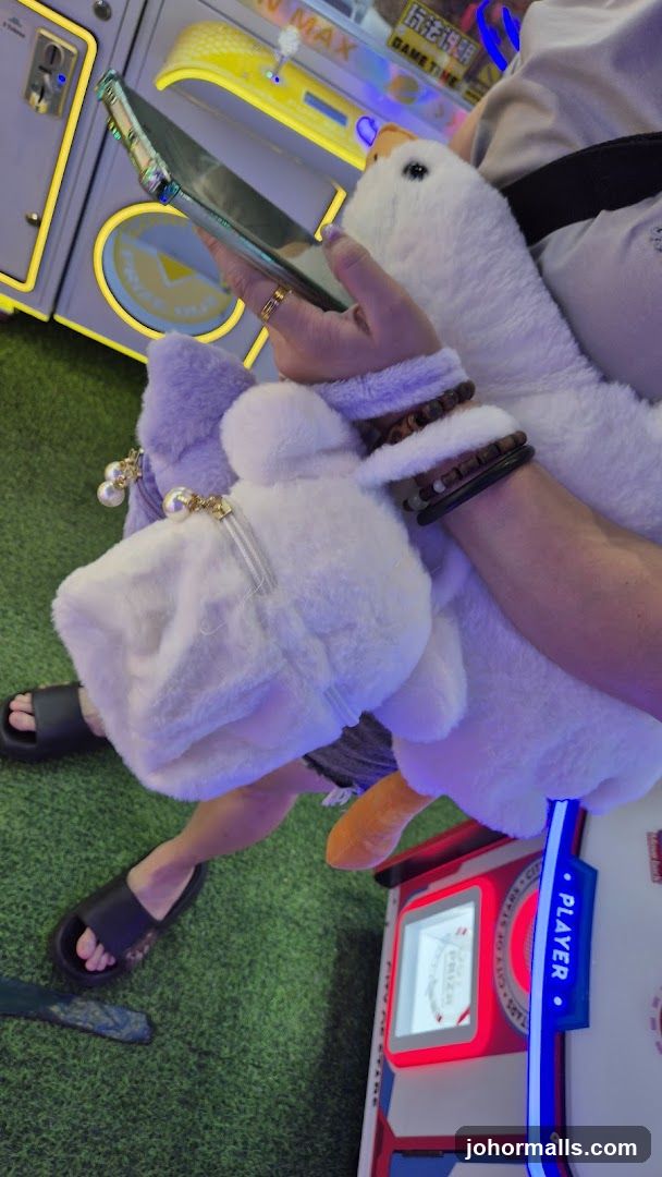 Person holding a plush toy and a phone near an arcade game