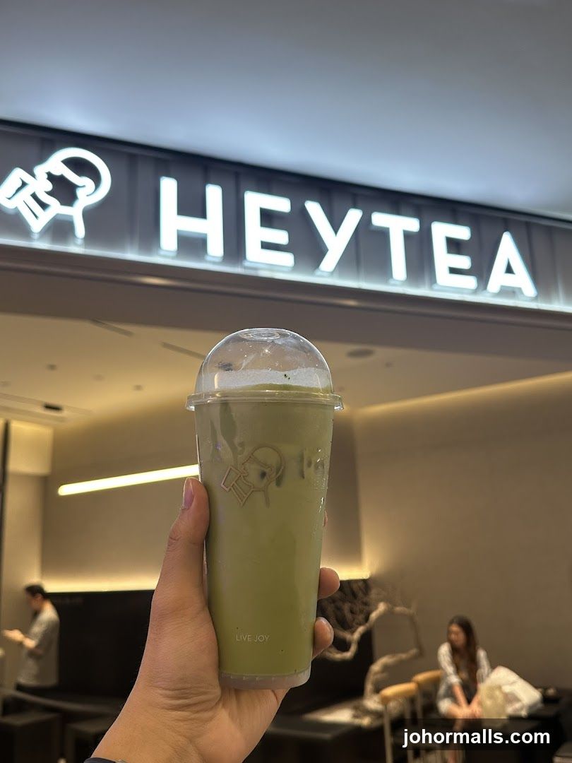 Person holding a matcha drink in front of a HEYTEA sign