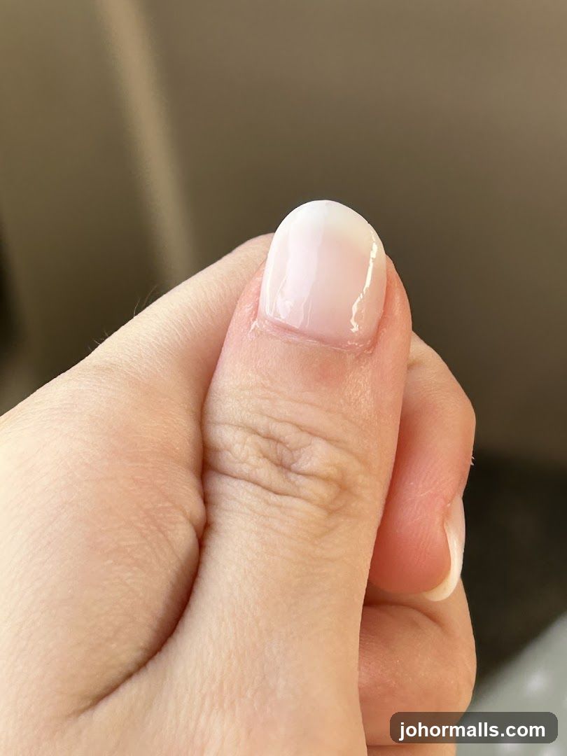 Close-up of a thumb with a sheer, milky white nail polish.