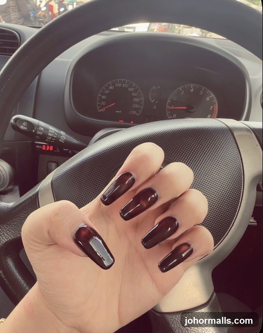 Hand with dark nails on car steering wheel