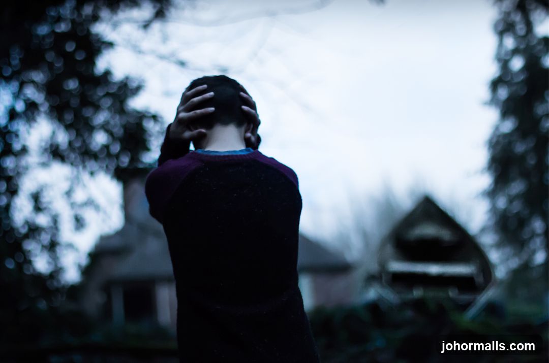 Person holding head in front of abandoned structures