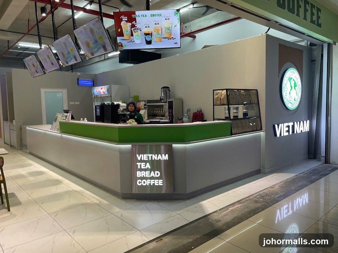 A view of the exterior of a Vietnam Tea Bread Coffee shop. The shop has a modern design with a white counter and green accents. There are digital menus displayed on screens above the counter, showing various drinks. A logo with the text "VINA TEA COFFEE" is visible on the wall. The shop's name, "VIETNAM TEA BREAD COFFEE," is also displayed prominently. A staff member is visible behind the counter.