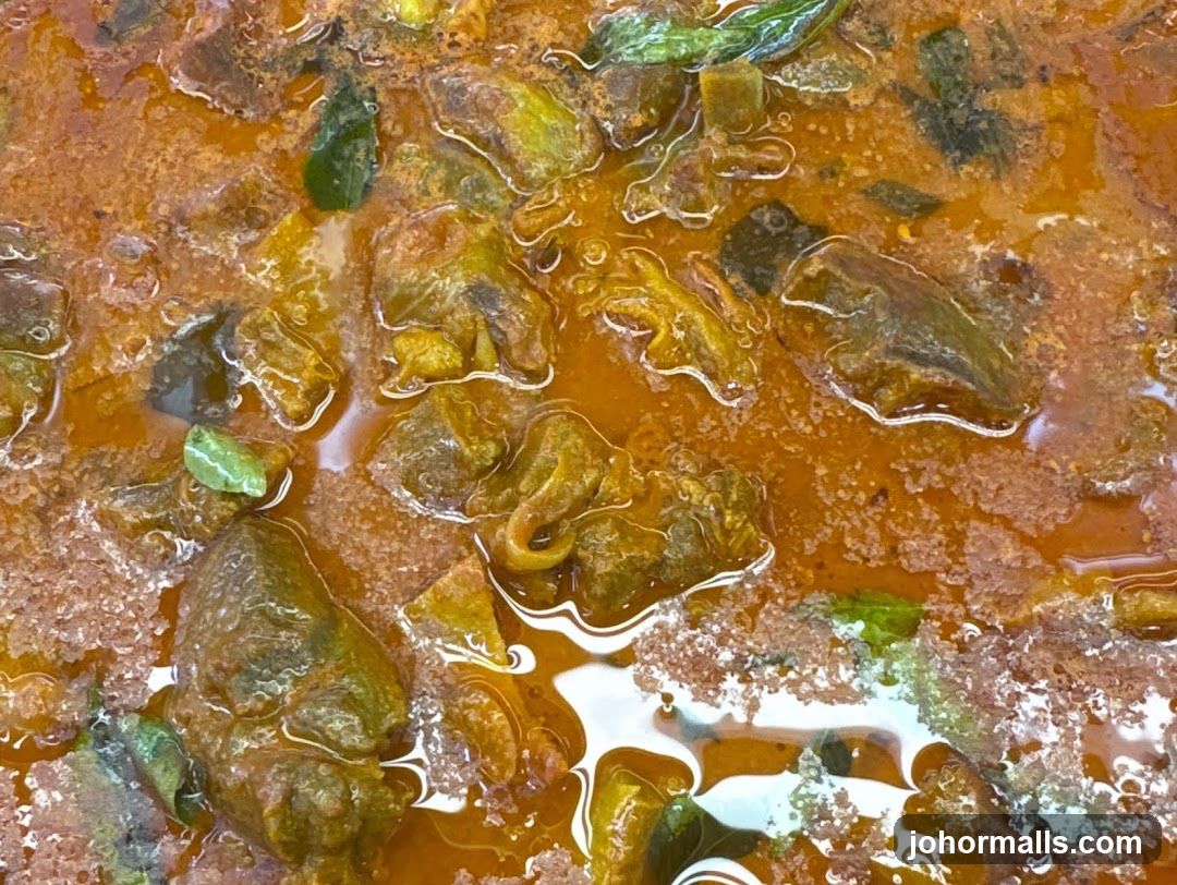 Close-up of a rich, orange curry with chunks of meat and green herbs.