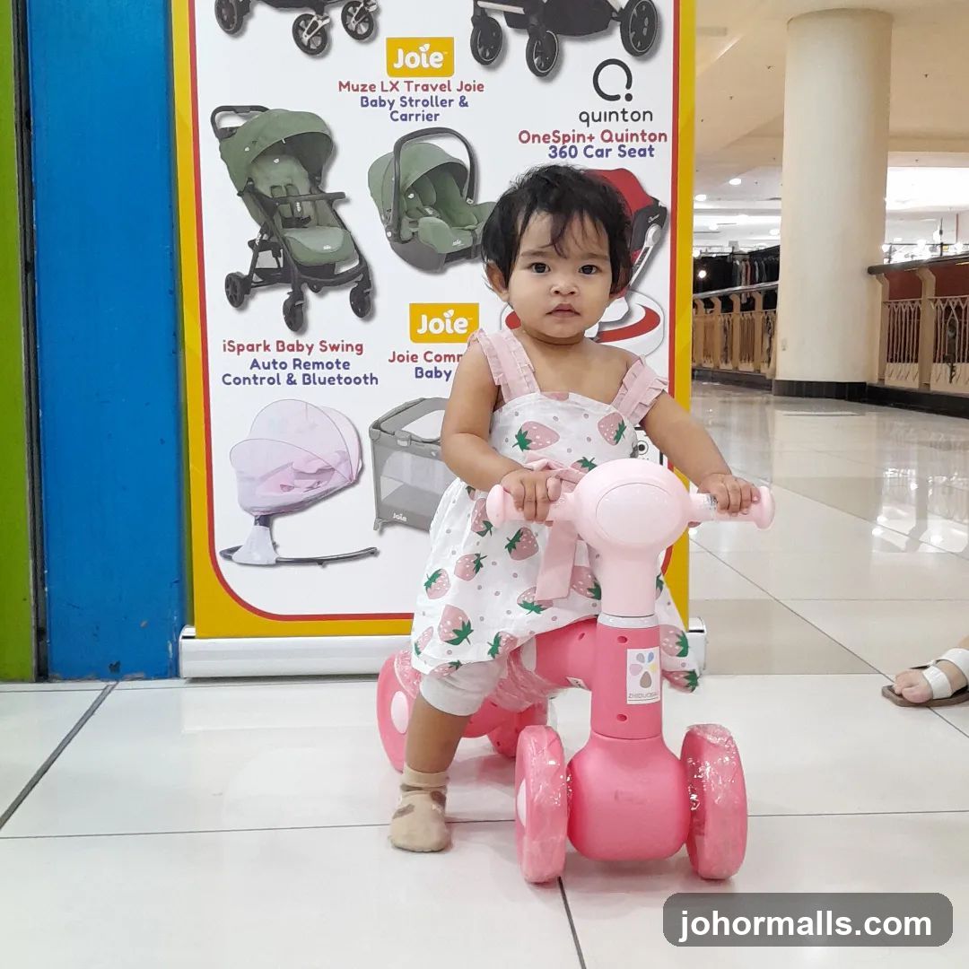 Child on a pink ride-on toy in front of a display of baby gear
