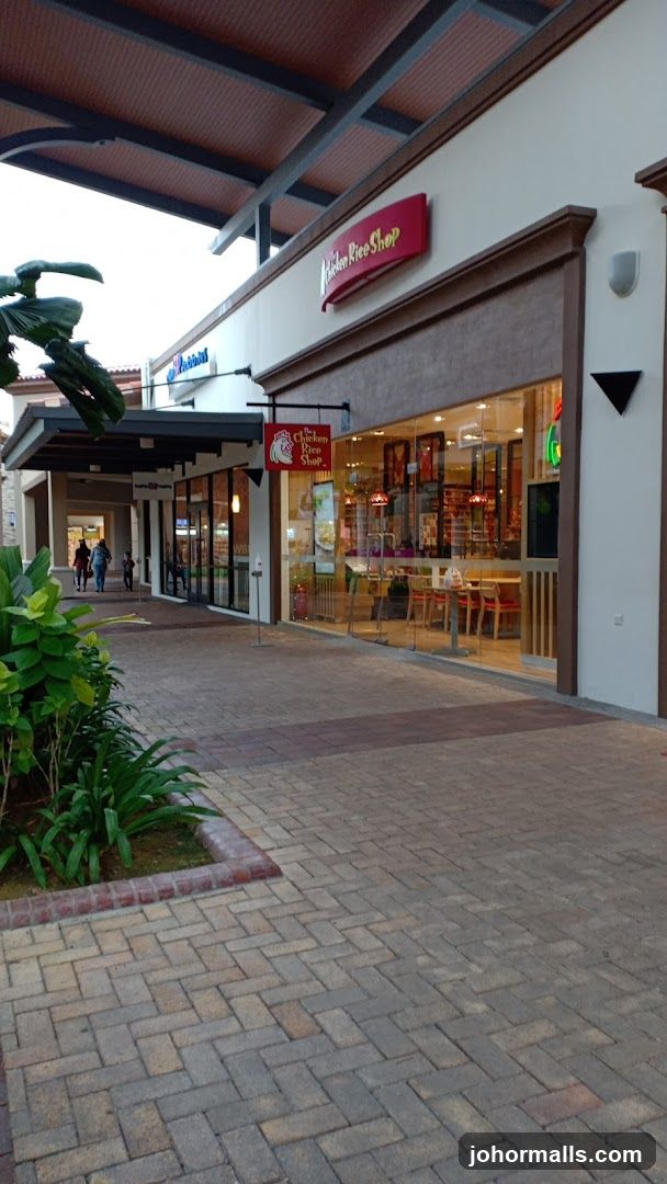 The exterior of a restaurant called "The Chicken Rice Shop" with large glass windows and a red sign above the entrance. The restaurant is part of a larger building with a covered walkway.