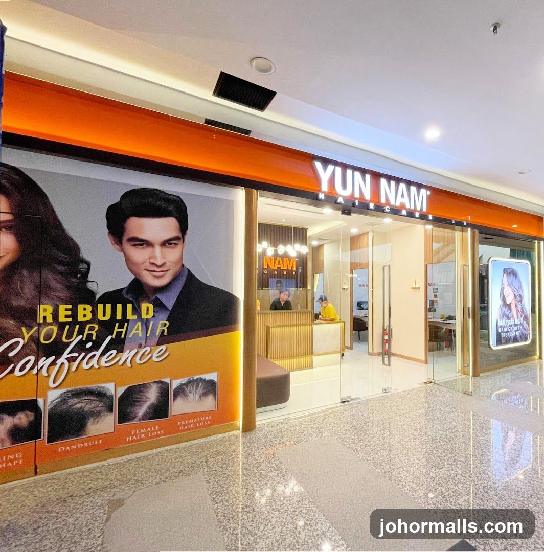 The exterior of a Yun Nam Hair Care salon. A large advertisement on the left features the text "REBUILD YOUR HAIR Confidence" and images illustrating hair conditions like dandruff, female hair loss, and premature hair loss. The salon entrance has glass doors and windows, with the "YUN NAM HAIR CARE" logo prominently displayed above the entrance. Inside, a reception desk is visible with staff members attending to customers.