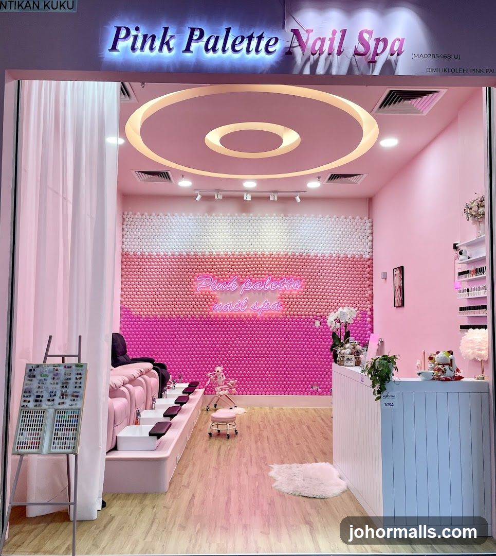 The exterior of a nail spa with a bright pink and white interior. The shop's name, "Pink Palette Nail Spa," is displayed in illuminated lettering above the entrance. Inside, there are pedicure chairs, a reception desk, and walls decorated with pink and white spheres. A display stand with nail polish samples is visible near the entrance.