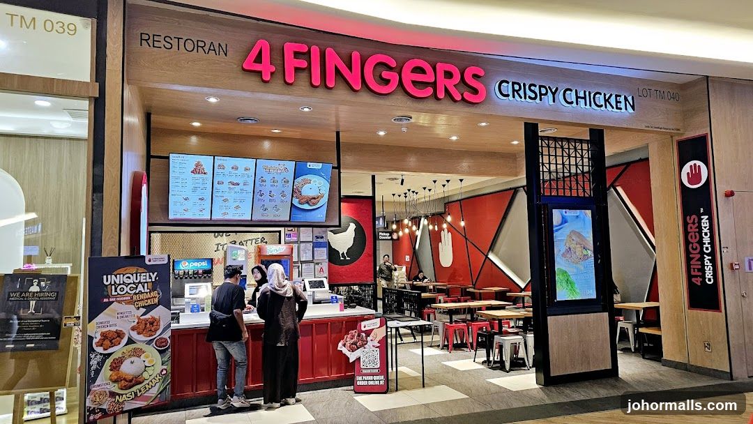 The exterior of a 4 Fingers Crispy Chicken restaurant. The storefront features a large neon sign with the restaurant's name and logo. Inside, tables and chairs are visible, along with a counter where customers are ordering. A menu board is displayed above the counter.