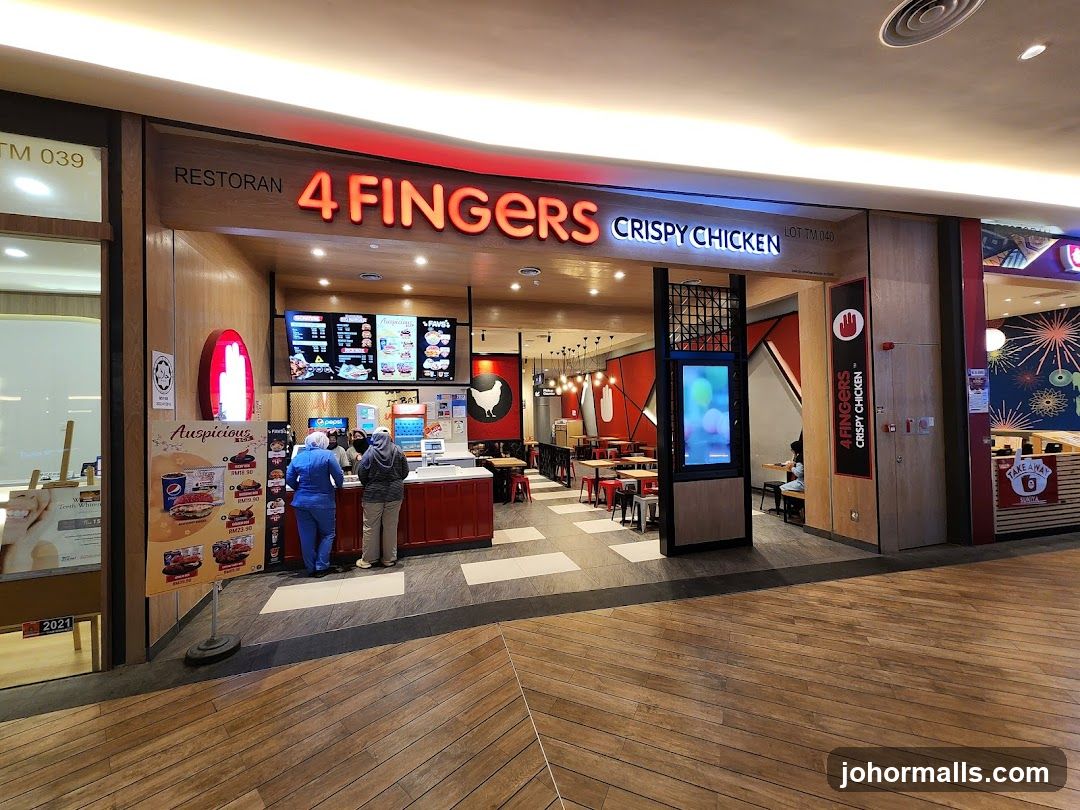 The exterior of a 4 Fingers Crispy Chicken restaurant. The restaurant has a large sign with the name "4 FINGERS CRISPY CHICKEN" in red neon letters. Inside, there are digital menus displaying food items and prices. Two customers are ordering at the counter, and staff members are visible behind the counter. The restaurant has red and wooden interior design elements, with tables and chairs set up for dining. A vertical sign with the restaurant's logo and name is also visible on the right side of the entrance.