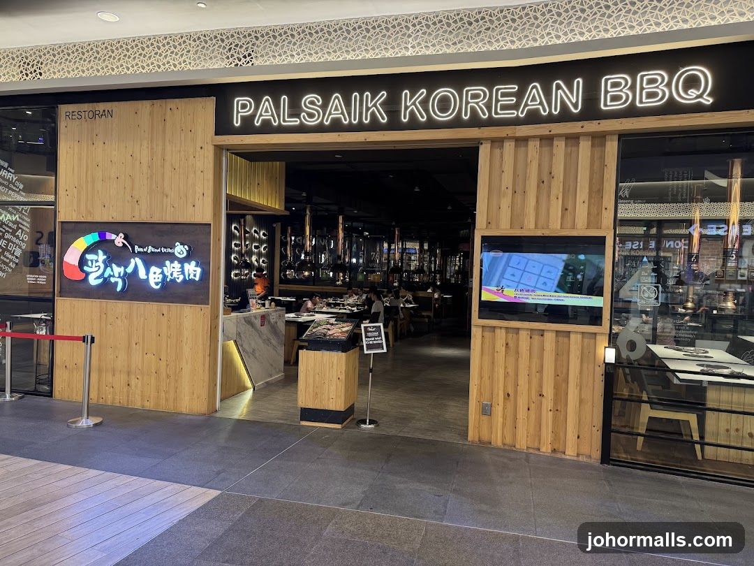 The exterior of a Korean BBQ restaurant with a wooden facade. A neon sign above the entrance reads "PALSAIK KOREAN BBQ". To the left, a colorful logo with Korean text is displayed. To the right, a digital screen shows a grid of images. The interior of the restaurant is visible through the entrance, showing tables and people dining.