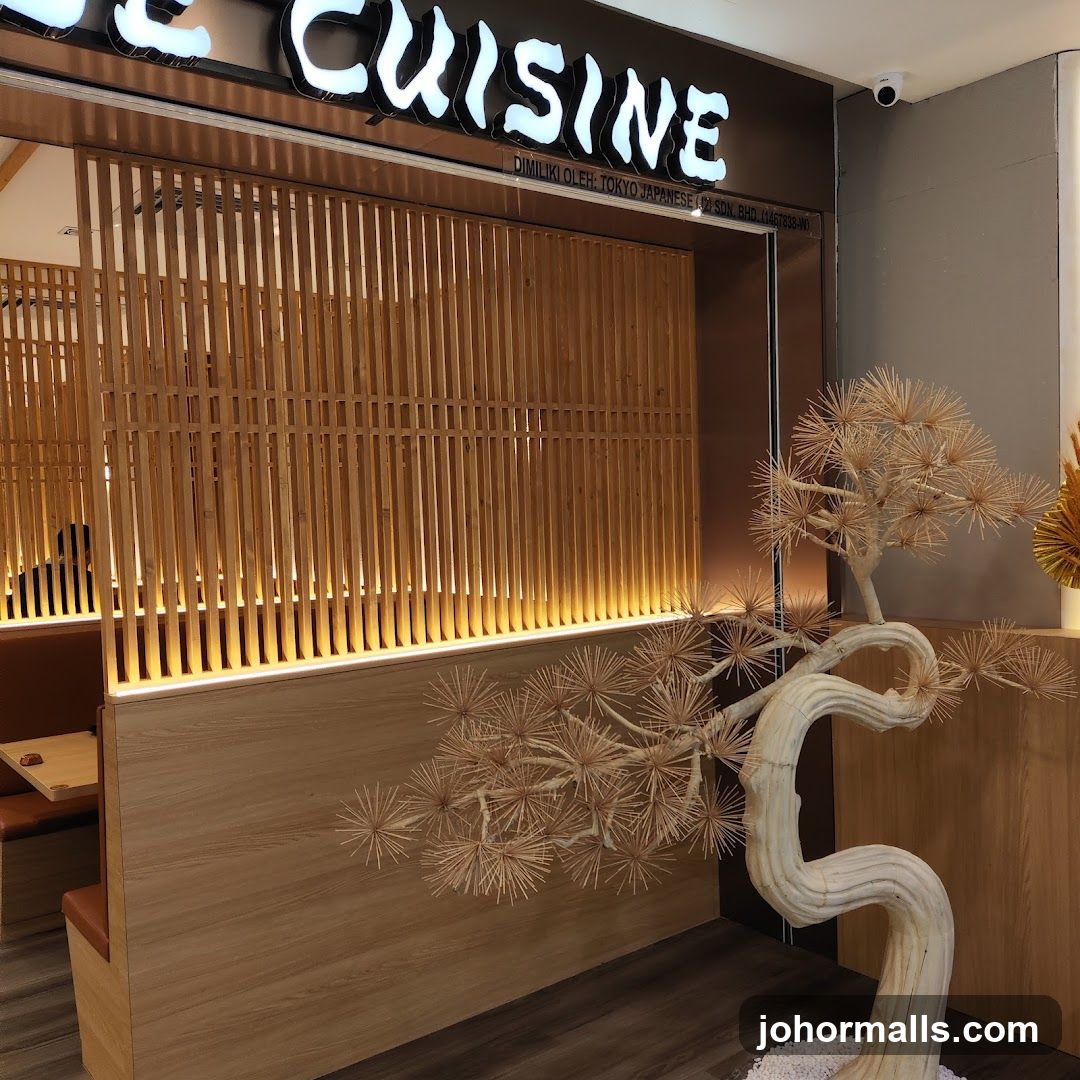 The exterior of a restaurant with a prominent "CUISINE" sign. The entrance features wooden slatted partitions and warm interior lighting. A decorative tree sculpture made of light-colored material and small white stones is placed in the foreground.