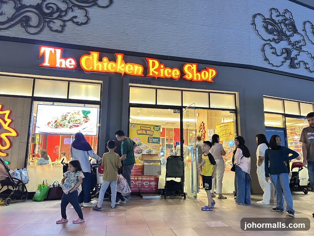 The exterior of a restaurant called "The Chicken Rice Shop". People are standing outside the entrance, some are looking at displays.
