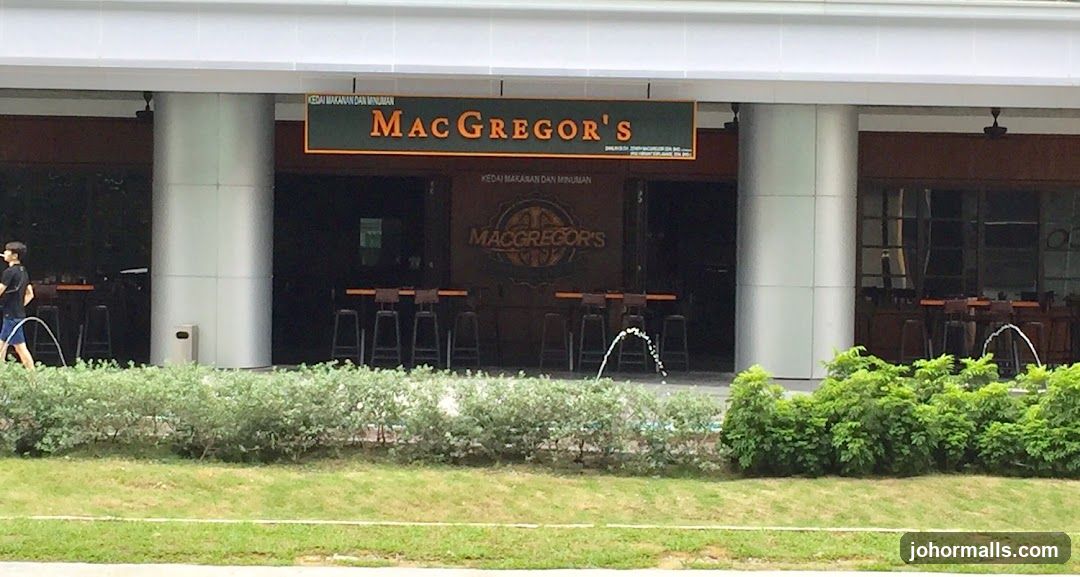 Exterior view of a modern building with large pillars and a dark brown facade featuring the 'MacGregor's' logo in gold lettering on a green sign above the entrance. Several high stools are lined up along the bar area inside, which is dimly lit. A person walks past on the left side of the frame. The foreground includes manicured bushes and grass.