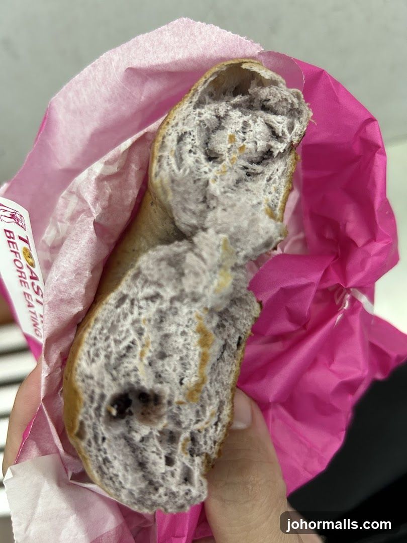 Hand holding a partially eaten bread roll wrapped in pink paper