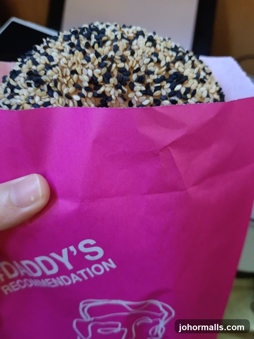 Hand holding a pink paper bag with a sesame-topped item