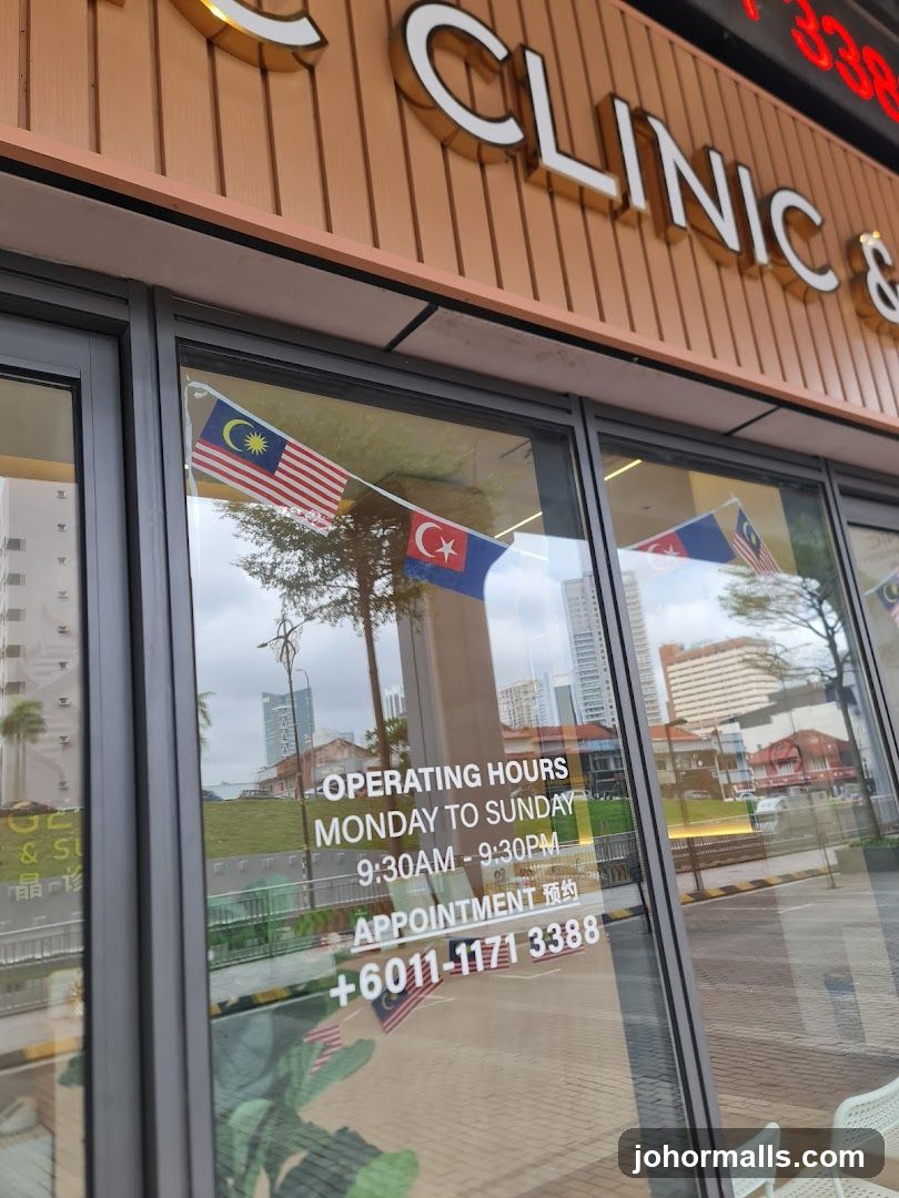 Exterior storefront with 'CLINIC &' sign in white letters on a brown panel. Glass windows display operating hours: Monday to Sunday 9:30AM–9:30PM, appointment line +6011-171 3388. Malaysian flags hang across the glass. Reflections show urban buildings and street scene. No menu or printed materials visible.