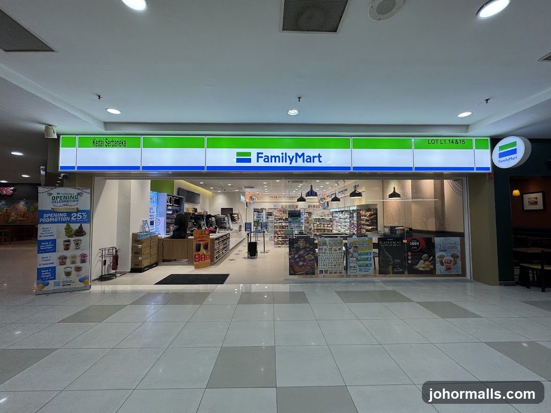 A FamilyMart store entrance with a green and white sign displaying "FamilyMart" and "Kedai Serbaaneka" above the doorway. The storefront is located in Lot L1:14&15. Inside, shelves are stocked with products, and promotional posters are displayed near the counter. A staff member is visible behind the counter. The floor has a tiled pattern, and ceiling lights illuminate the space.