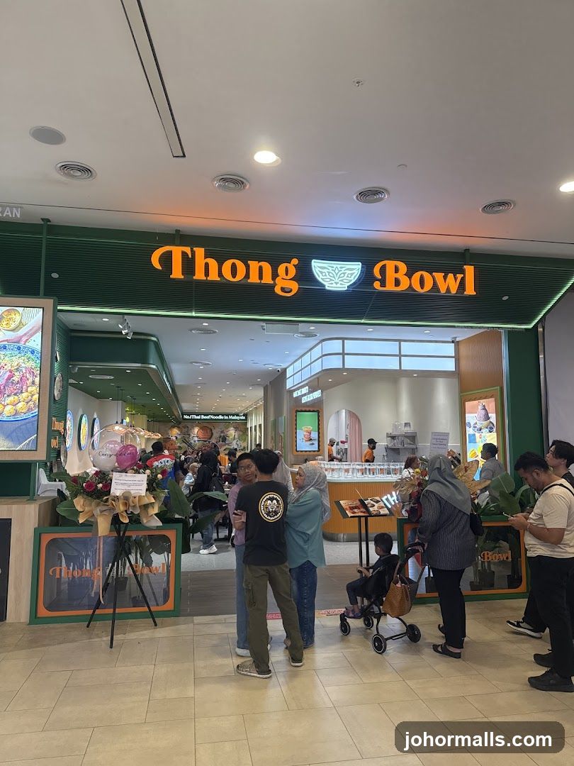Storefront with illuminated orange signage reading 'Thong Bowl' above a green facade; customers queue inside the entrance; promotional floral arrangement on stand to left; interior shows bright lighting and modern design.