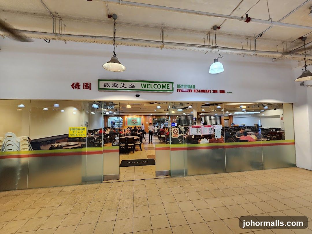 Storefront with glass facade showing interior dining area; sign above reads 'WELCOME' in English and Chinese, with business name 'Evergreen Restaurant Son. Bhd.' to the right. Visible inside: patrons seated at tables, staff moving about, tiled floor, hanging lights, and a yellow 'BUSINESS HOURS' sign on left side of entrance. No menu board or printed material clearly visible.