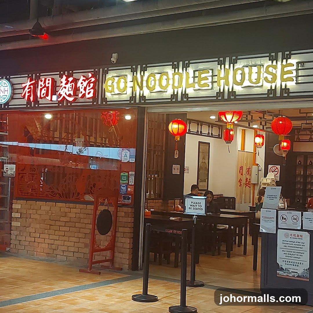 The exterior of a noodle restaurant with a prominent sign reading "有間麵館 GO NOODLE HOUSE". Red lanterns hang outside the entrance, and brickwork is visible on the lower facade. Inside, tables and chairs are set up, and patrons are seated.