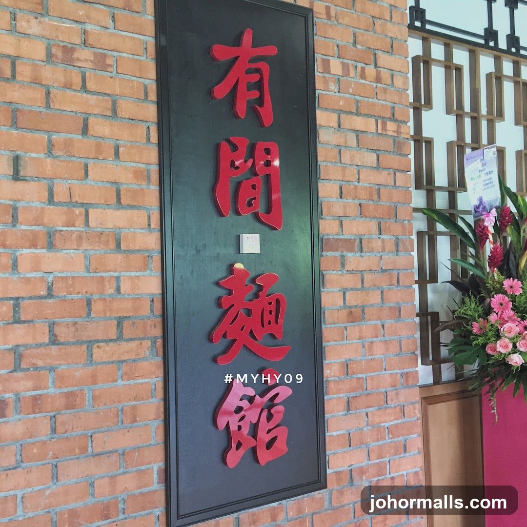 A vertical black sign with red Chinese characters is mounted on a brick wall. Below the characters, the hashtag #MYHY09 is visible. To the right of the sign, a decorative floral arrangement is placed next to a wooden lattice screen.