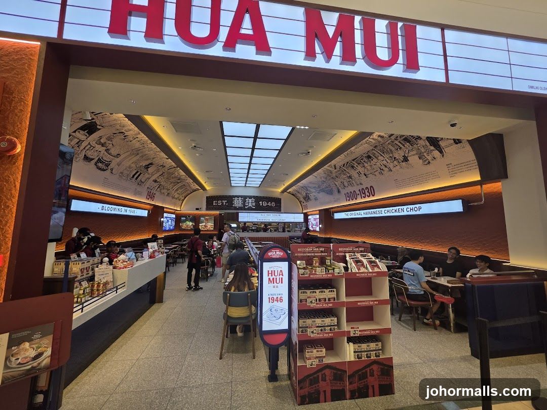 The exterior of a restaurant with a large sign that reads "HUA MUI". The restaurant has a modern interior with seating areas and a counter. There are displays of packaged food items and historical murals on the walls.
