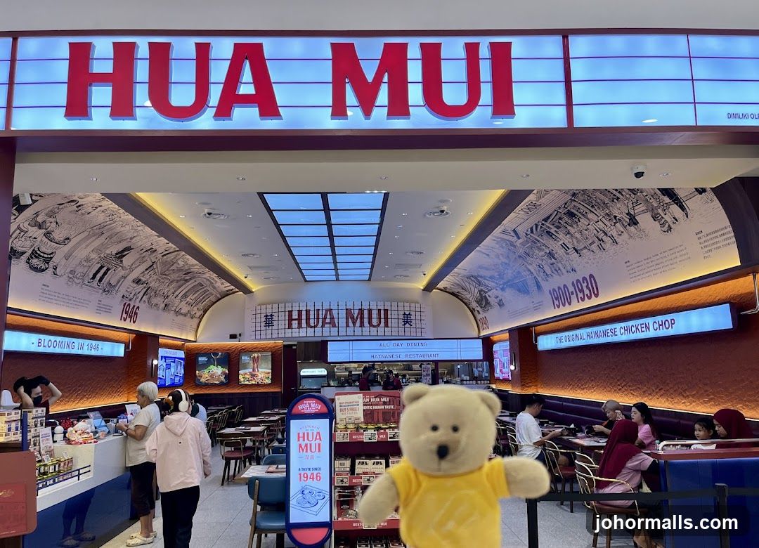 The exterior of a Hua Mui Hainanese Restaurant with large red lettering spelling out "HUA MUI" above the entrance. The interior is visible, showing tables, chairs, and patrons dining. Decorative murals depicting historical scenes and dates like "1946" and "1900-1930" adorn the walls. A sign highlights "THE ORIGINAL HAINANESE CHICKEN CHOP." A plush bear toy in a yellow shirt is in the foreground.