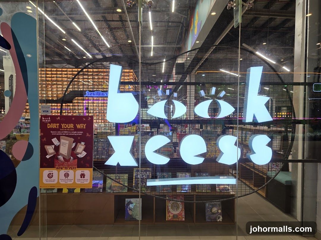 A glass storefront with the store name "Book Xcess" displayed in large, illuminated blue letters. Below the name, shelves are visible displaying books and other merchandise. A promotional poster titled "DART YOUR WAY" is also displayed on the left side of the entrance.