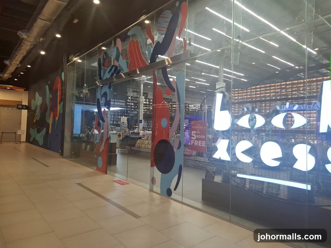 A view of a bookstore's entrance with large glass windows. The windows have colorful abstract art decals and large illuminated text that reads "book aces". Inside, shelves filled with books are visible, along with a counter and some staff members. A sign on the window advertises "4 BOOKS & 5TH BOOK FREE".