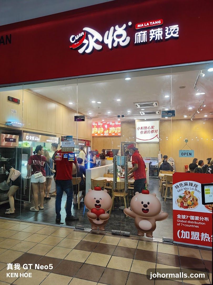 The exterior of a Cuan Ma La Tang restaurant with a red awning and large glass windows. Inside, customers are seated at tables and staff are serving food. Two cartoon bear figures are visible on the glass doors. A sign on the right advertises "MIX Ma La Ban" and "Global distribution of 7+ countries."