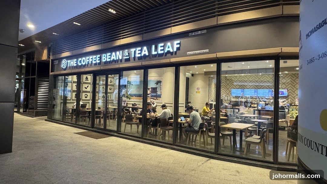 The exterior of a "The Coffee Bean & Tea Leaf" cafe. The storefront features large glass windows and doors, with the cafe's name prominently displayed in illuminated lettering above the entrance. Inside, tables and chairs are visible, with customers seated and enjoying their time. The interior is well-lit and appears to be a comfortable space for patrons.